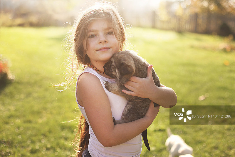 女孩抱着棕色的小狗，站在草坪后院的阳光下图片素材