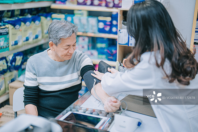 亚洲华人女药剂师与高级男子在药店测量血压图片素材