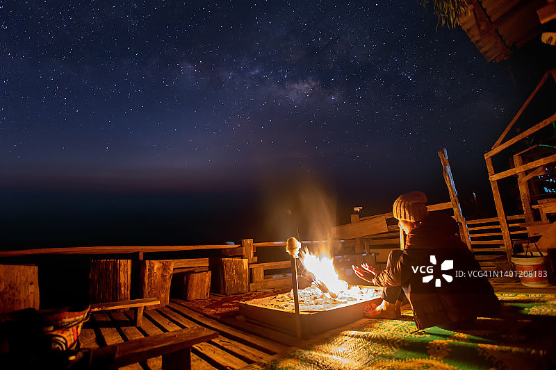夜空下的篝火伴着星星和银河。晚上露营。徒步旅行的游客在她的营火中休息图片素材