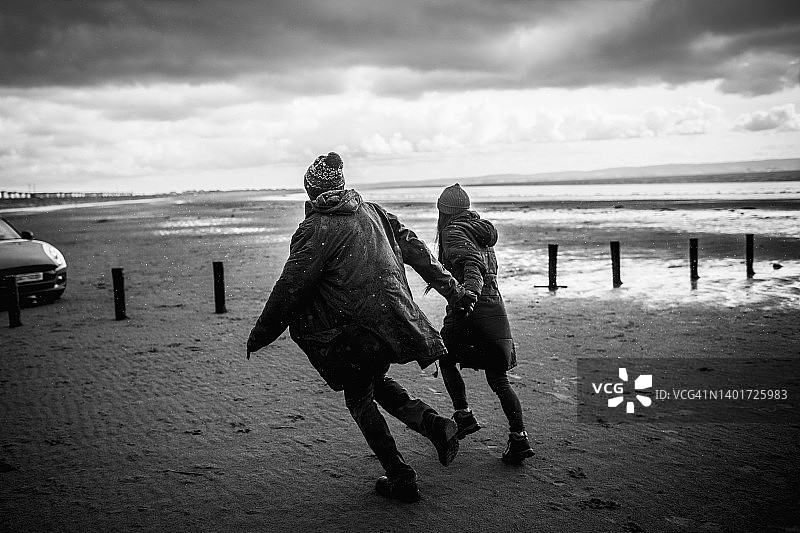 在冬季沙滩上牵手奔跑的情侣图片素材