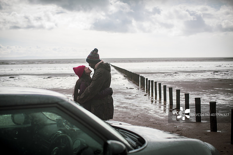 一对深情的情侣在潮湿的冬季海滩上拥抱图片素材