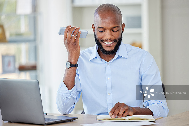 年轻的非洲裔美国商人一边打电话一边在笔记本上读笔记，在办公室里用笔记本电脑工作，独自工作。一名男性商务人士一边工作一边打电话图片素材
