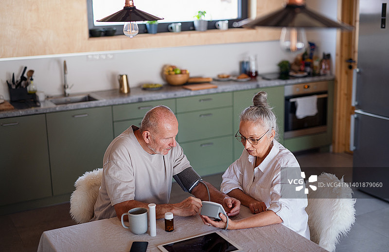 老年夫妇坐在厨房，测量血压，吃药的高角度视角。图片素材