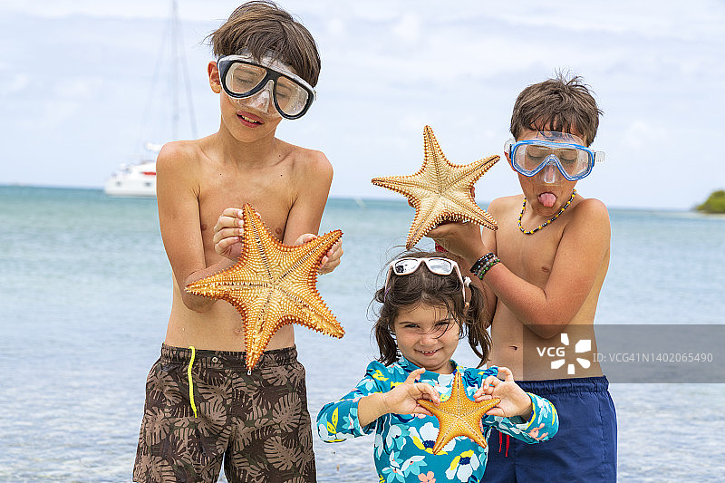 戴着潜水面罩的快乐孩子们在海滩上展示海星图片素材