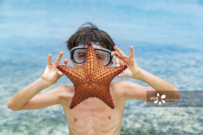 戴着潜水面罩的小男孩在海边抱着一只海星图片素材