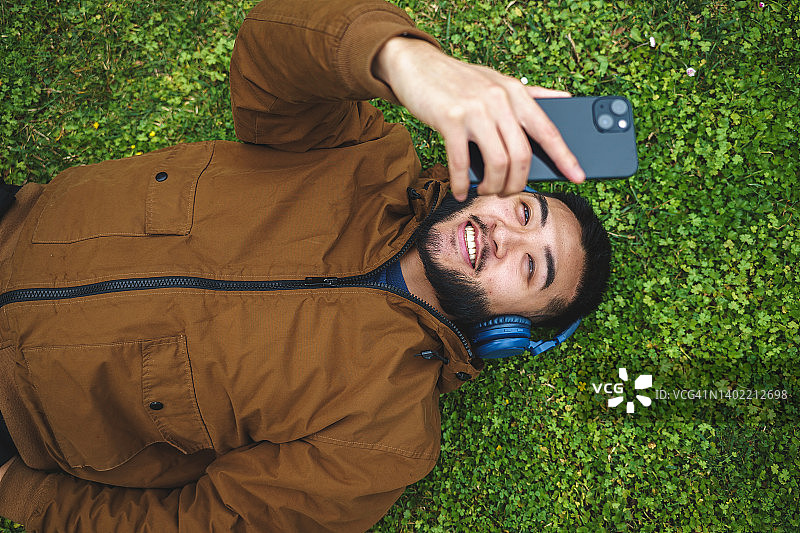快乐的民族男子戴着耳机在智能手机上自拍图片素材