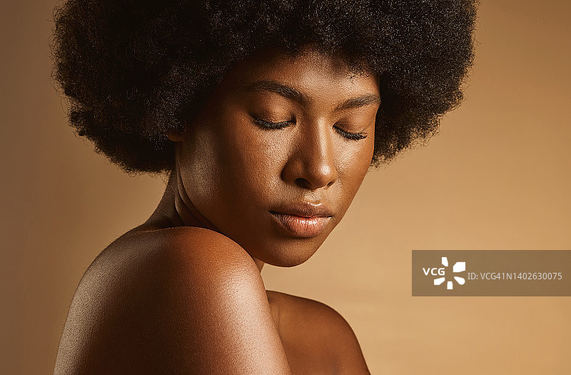 美丽的非洲裔美国女人与爆炸头和发光的皮肤在一个棕色的工作室背景摆姿势。年轻女子化妆自然，看起来完美而自信图片素材