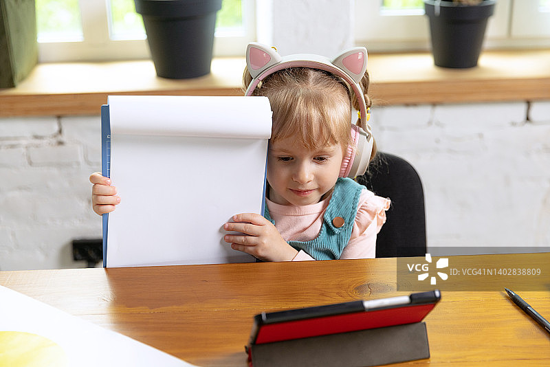 可爱小女孩的真人肖像，学龄前儿童靠在家里使用数码平板电脑。教育、童年、人、作业和学校观念。图片素材