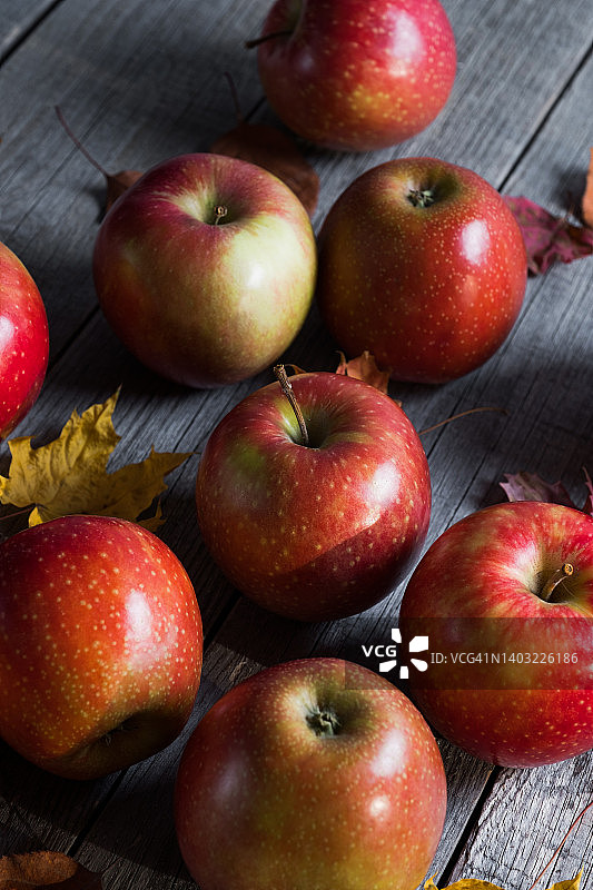 红色的苹果和秋天落叶的桦树，枫树和白杨在木制背景。水果在厨房的桌子上。种植有机农产品。素食的概念，纯素，生食和饮食。秋天的自然背景。收割。图片素材