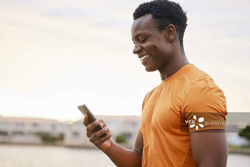 一个健身男子微笑着看着他的手机。一个穿着运动服的非洲裔美国人在查看他的智能手机。图片素材
