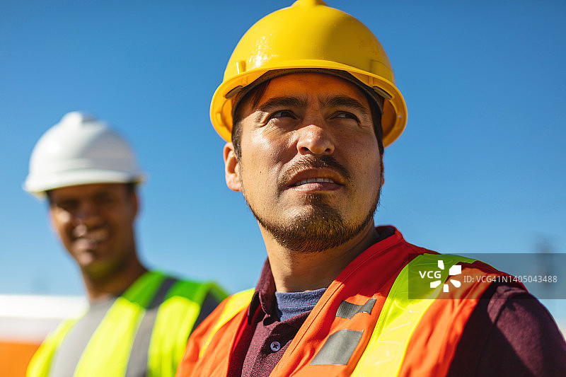 在工地上穿着PPE的黑人和西班牙裔男性建筑工人评估和讨论项目基础设施系列照片图片素材