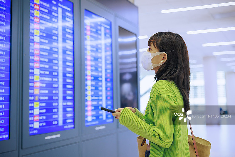 年轻的亚洲女商人戴着口罩在机场的登机牌上写着字。商务旅行的概念。图片素材