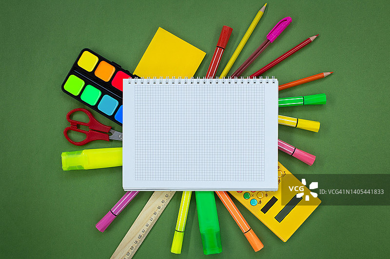 绿色背景的笔记本周围的一套文具。钢笔，马克笔，记号笔，剪刀，计算器，颜料。回到学校概念。本空间图片素材