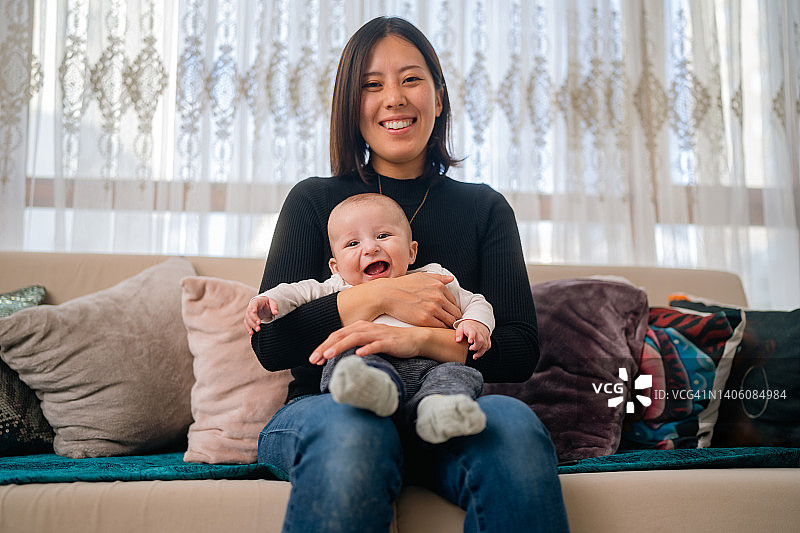 幸福的母亲和她的小婴儿坐在沙发上的肖像在家里客厅图片素材