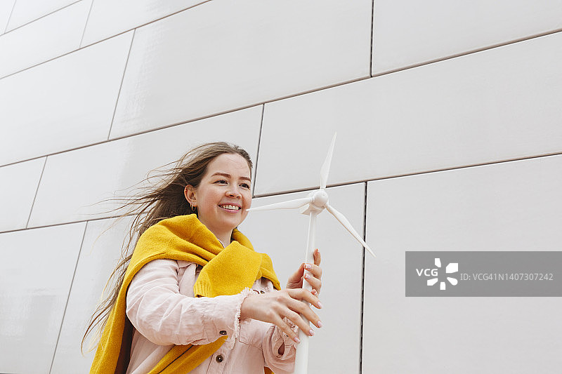 快乐的女人和风力涡轮机模型站在墙前图片素材