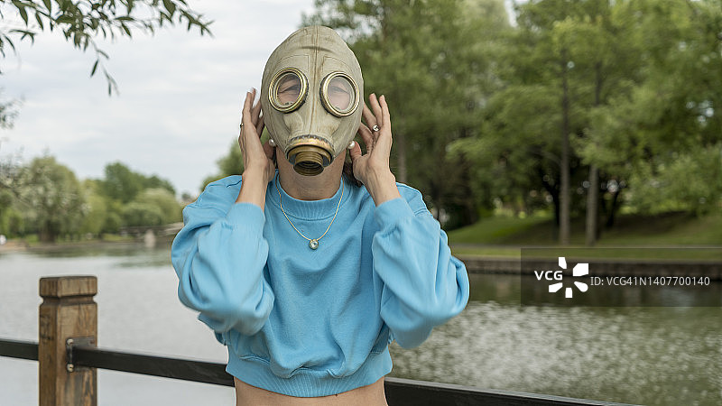 女孩在河岸上戴上了防毒面具。城市中的疏离感。时尚、生态、孤独的概念。图片素材