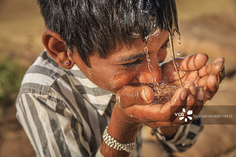 印度拉贾斯坦邦，沙漠村庄，小男孩喝着淡水图片素材