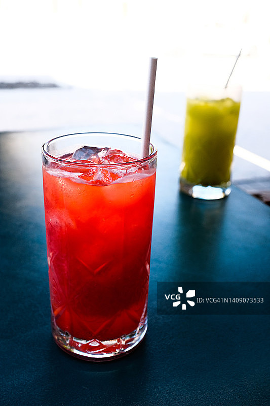 草莓浆果软饮料或加冰鸡尾酒，用吸管喝在玻璃杯子在户外咖啡馆或餐厅的木桌上。在炎热、闷热的夏天喝的清凉饮料。图片素材