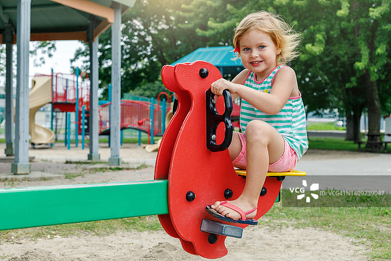 夏天小孩子在操场上玩，坐在跷跷板上。女孩在公园里玩。快乐的童年图片素材