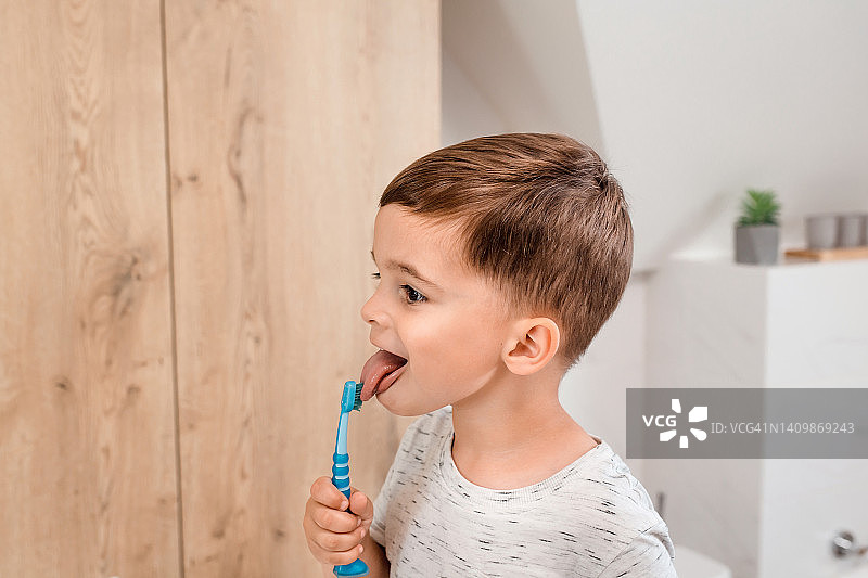 阳光明媚的早晨，小男孩在现代化的浴室里开心地刷牙。儿童牙齿卫生及健康图片素材