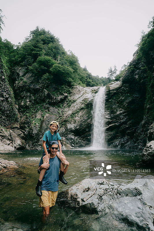 父亲扛着孩子走在瀑布前图片素材