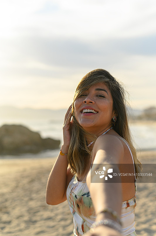 年轻微笑的女孩穿着裙子在海滩上自拍。女人在沙滩上自拍的概念。图片素材