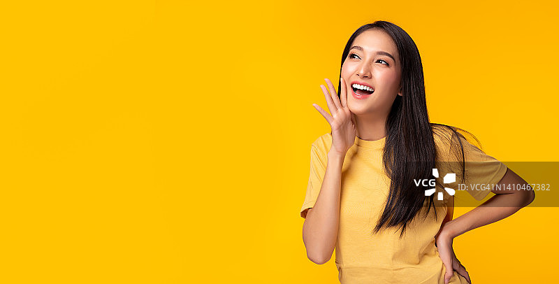 惊讶快乐的亚洲女人在兴奋地看着拷贝空间表情丰富的面部表情呈现产品漂亮的女孩像一个告诉客户孤立在黄色背景拷贝空间图片素材