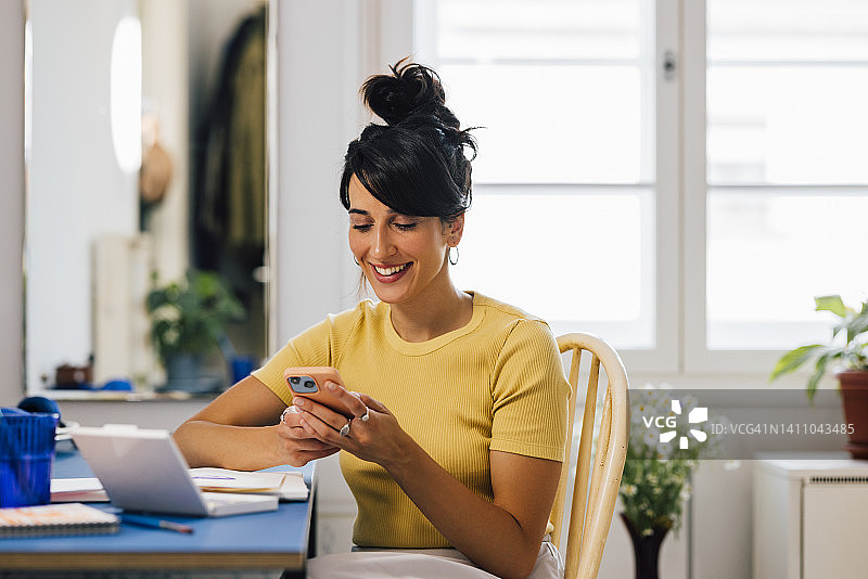 一名微笑的白人女商人穿着随意，坐在家里用手机发短信图片素材
