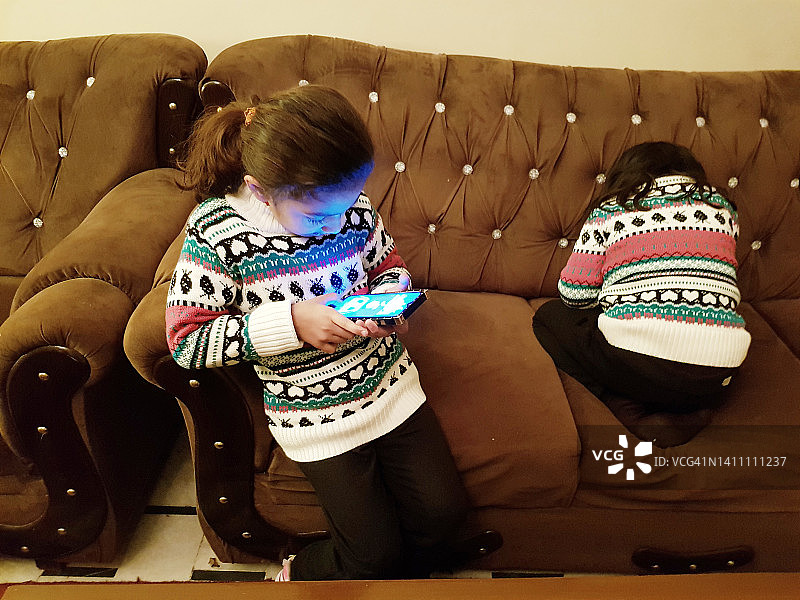 两个小妹妹在客厅里忙着用自己的手机。图片素材