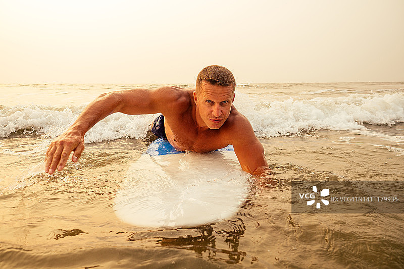 冲浪自由职业者肌肉和新闻运动训练在海滩日落。在印度洋goa Ashwem Arambol海滩附近，一个大冲浪板的男性健身模型冲浪图片素材