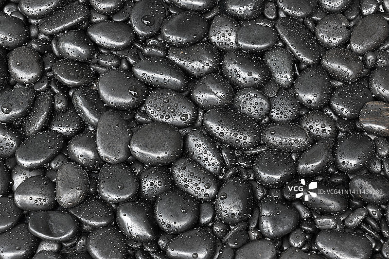 黑色鹅卵石的纹理和背景光滑的天然沙滩石头或岩石和水滴。图片素材