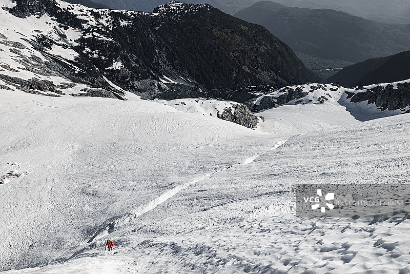 一个登山运动员走在积雪覆盖的大冰川上，山谷在远处图片素材