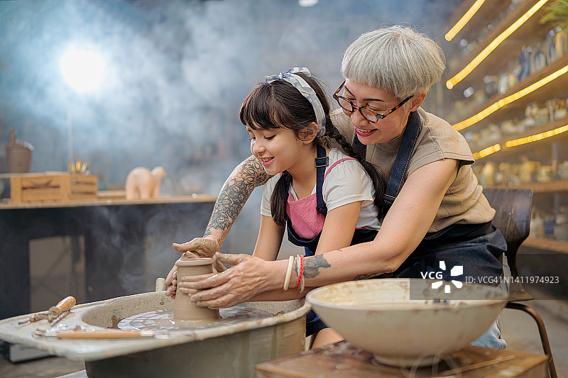 高级女艺术家在教小女孩在陶器轮上制作陶器。图片素材