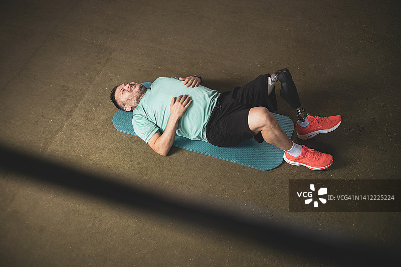 一位戴着假肢的残奥会运动员在地板上锻炼腹肌。残疾人。图片素材
