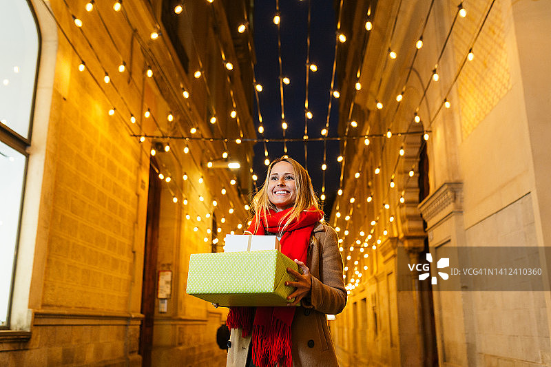 黄昏时分，年轻女子背着圣诞礼物穿过城市。图片素材