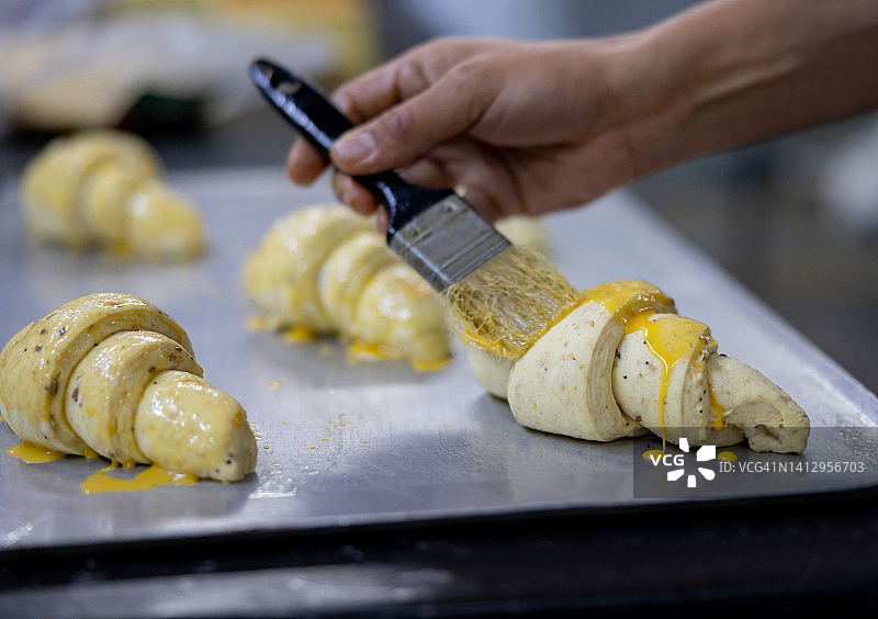 一个面包师在面包上撒蛋黄的特写图片素材