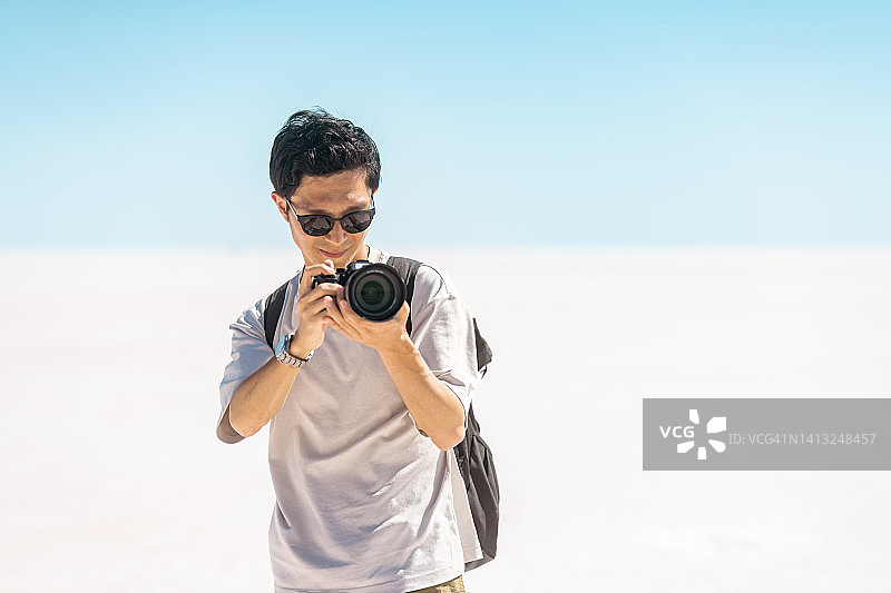 年轻的男性游客在盐湖的白盐上用相机拍摄视频和照片图片素材