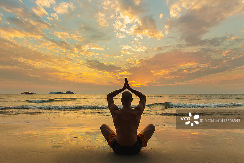 运动男子在日落时在海滩上以莲花姿势冥想。自我护理和心理健康。图片素材