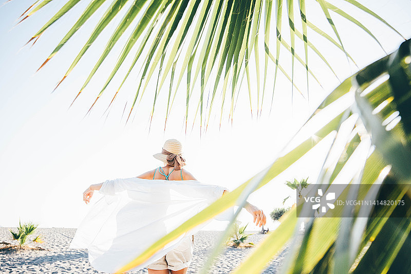 快乐的女人走在棕榈树附近在一个夏日阳光明媚的日子。图片素材