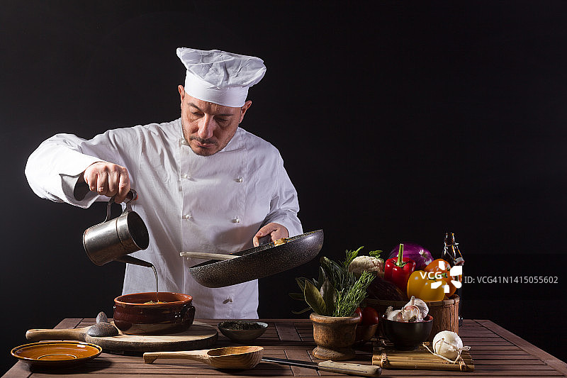 男厨师身穿白色制服，戴着帽子，将橄榄油倒入盛有蔬菜的锅中图片素材