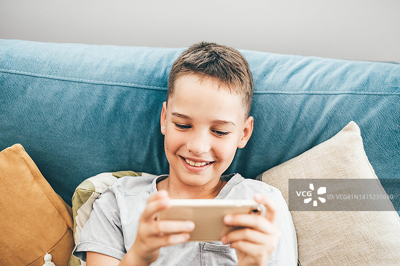 小男孩在家用手机玩电子游戏。男孩使用智能手机时看起来很惊讶。图片素材
