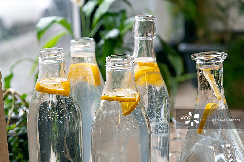 一种清凉的夏季饮料或鸡尾酒，放在醒酒器中。清洁水或柠檬柠檬片在玻璃醒瓶。透明的酒杯旁，木桌上，夏日艳阳高照闷热的日子。图片素材