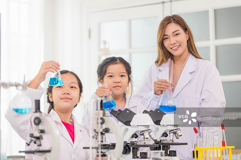 小学科学课上，活泼的小朋友和科学老师一起在学校实验室展示装有化学液体的测试瓶，科学实验室图片素材