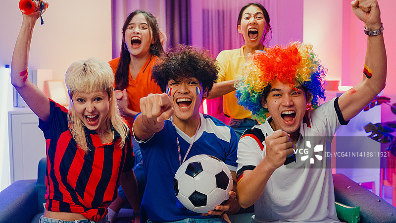 一群快乐的亚洲青少年坐在沙发上观看欢呼运动，足球比赛，世界杯冠军在晚上。图片素材
