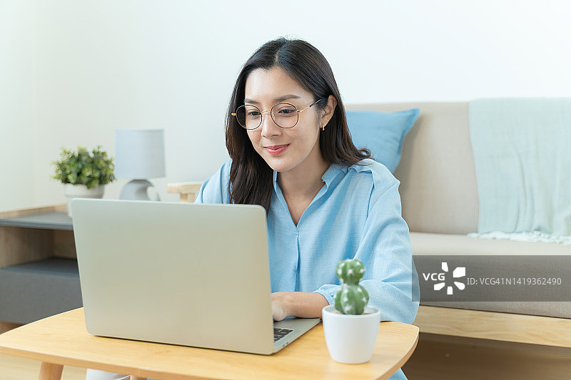 亚洲女性在家使用笔记本电脑工作。图片素材