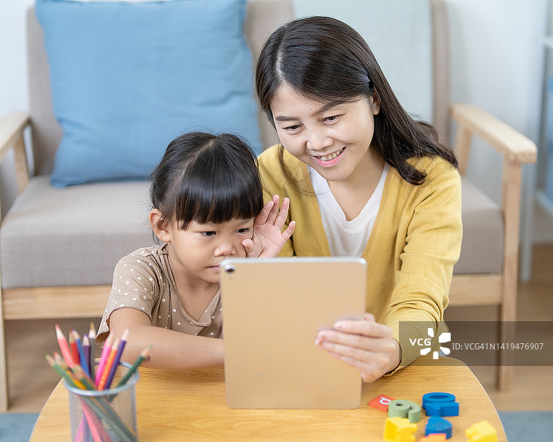 微笑的亚洲女学生在线学习平板电脑和母亲帮助她在家里图片素材