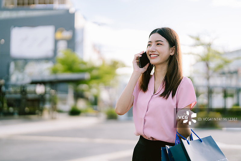 一名年轻女子在城市里购物，一边看手机一边微笑。图片素材