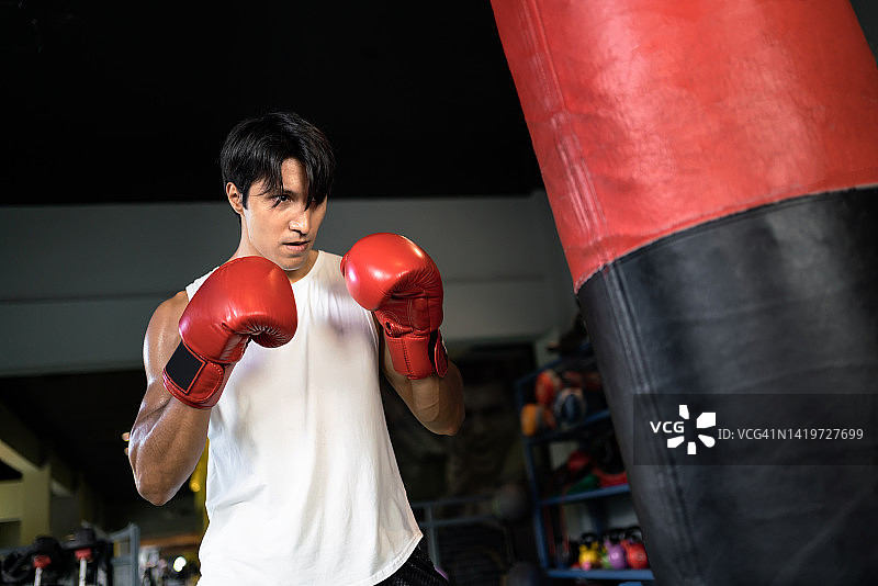 亚洲男人在健身房用沙袋练习拳击图片素材