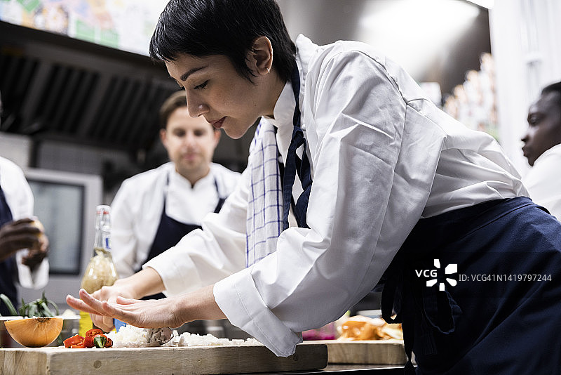 女厨师在商业厨房工作时切洋葱的侧面图图片素材