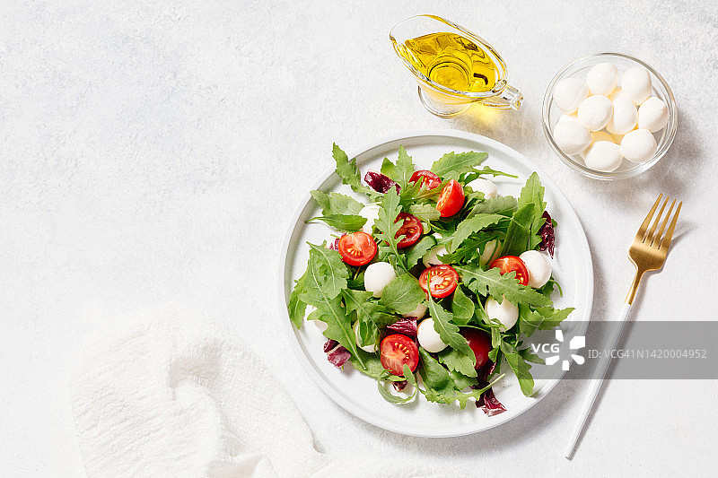 新鲜的蔬菜沙拉由马苏里拉奶酪，圣女果，芝麻菜和橄榄油制成，白色的石头桌子的背景。健康饮食理念。平铺，俯视图，拷贝空间。图片素材